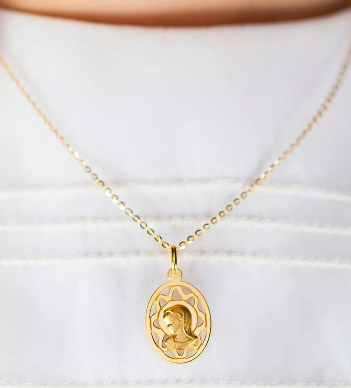 medalla religiosa de oro virgen niña ovalada y calada sobre traje de comunion